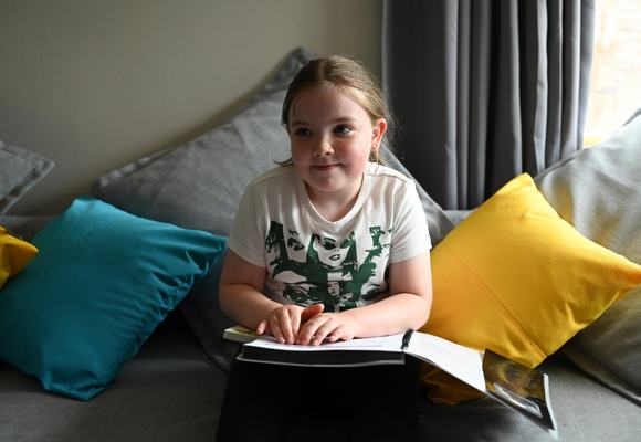 A young girl sitting on a sofa reading a book