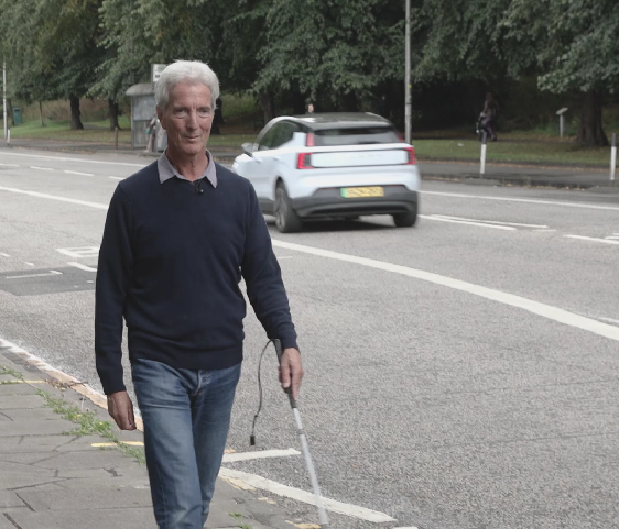 Ken walks down the street with his white cane.