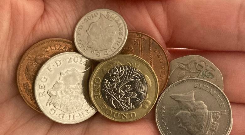 A close up of a collection of coins of different denominations (£1, 20p 10p and 2ps) in a person's palm