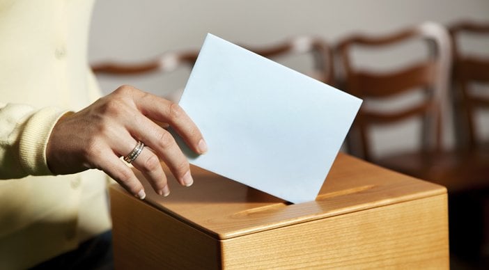 A person dropping a piece of paper into a ballot box